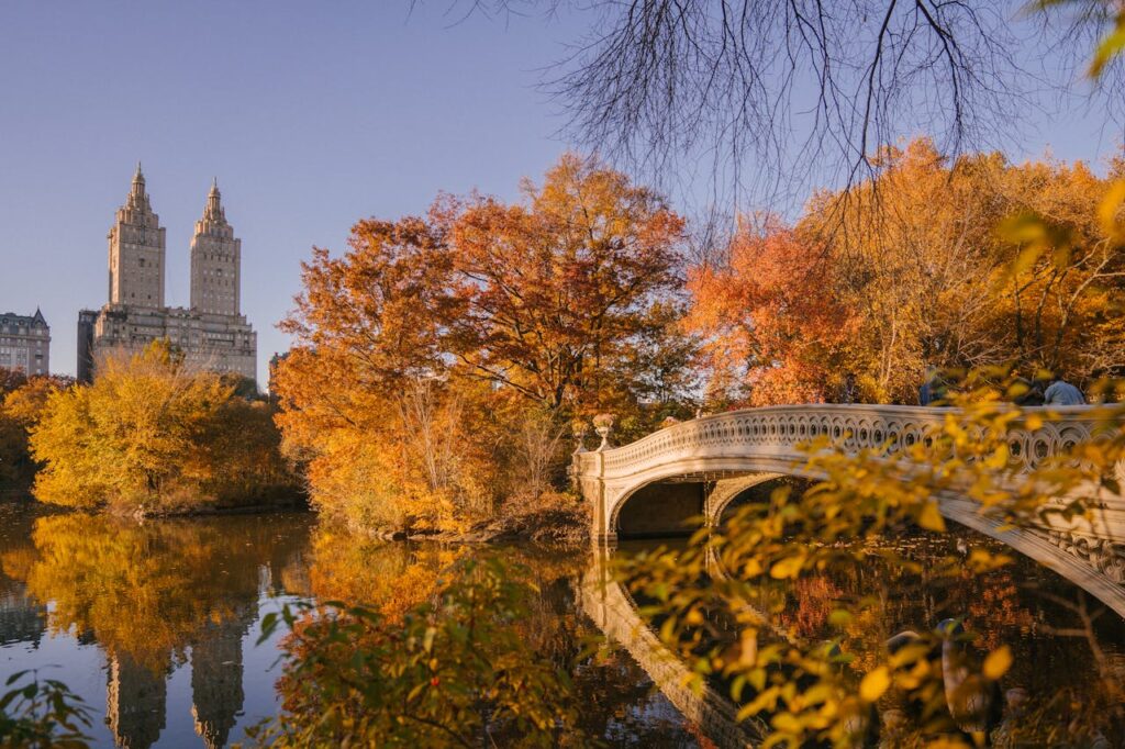 Bow Bridge crossing calm lake in autumn park